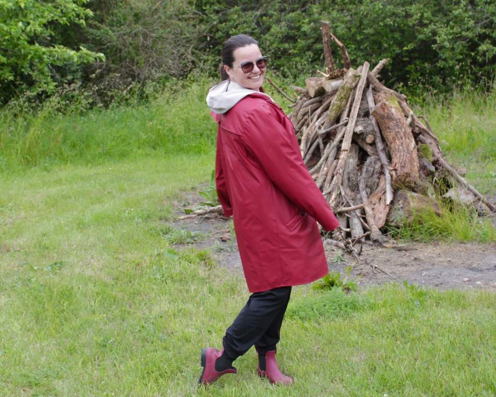 Hannah Brown, founder of Sounds & Stories, in front of an unlit bonfire in the countryside of Muhu island, Estonia wearing in a red raincoat and red gumboots